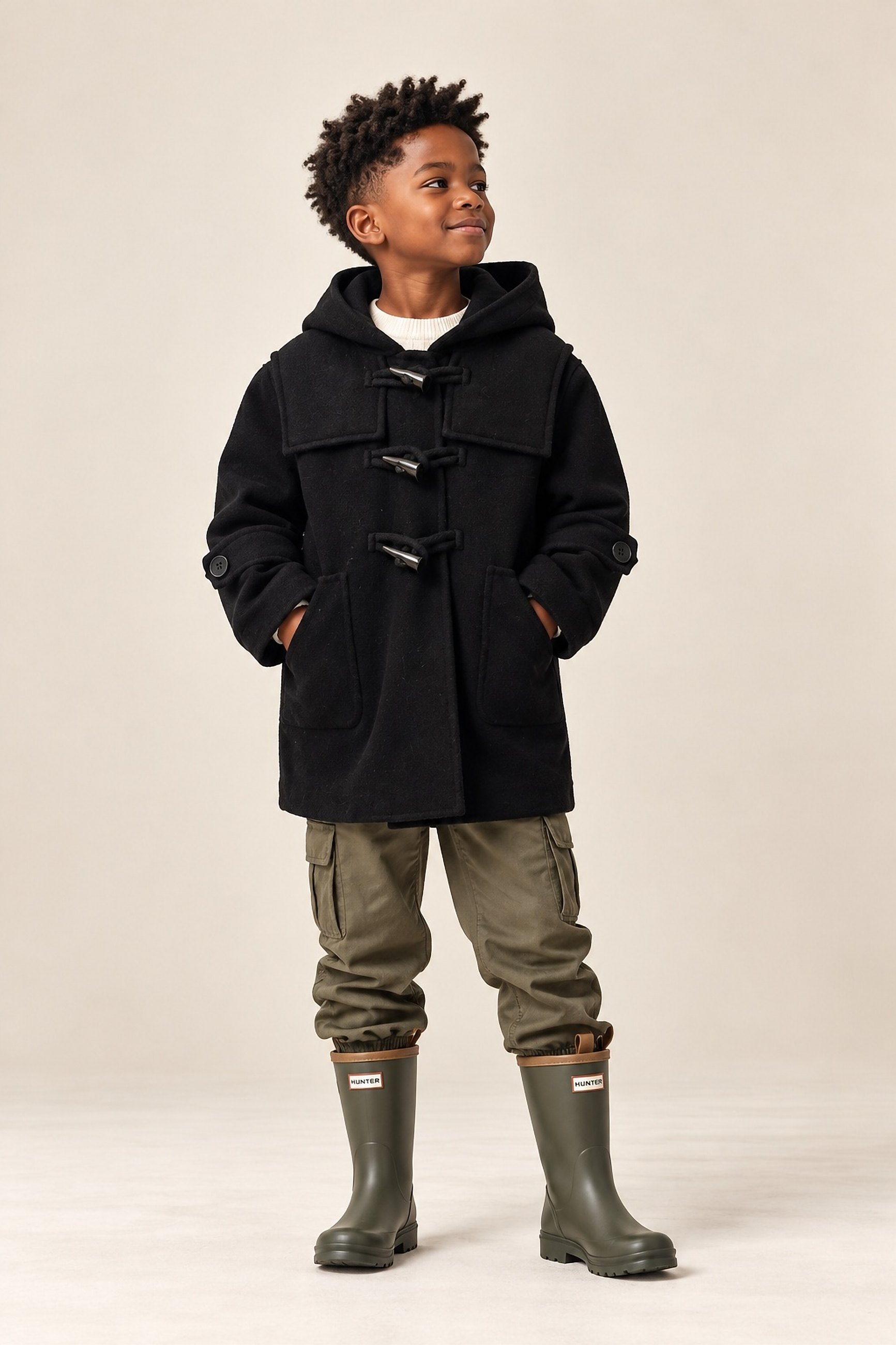 A boy in the black hooded duffle coat with cargo trousers and rain boots